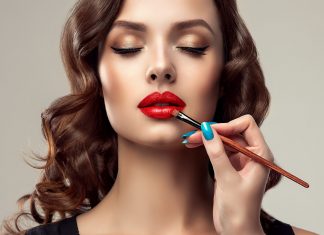 Makeup artist applies red lipstick . Beautiful woman face. Hand of make-up master, painting lips of young beauty model girl . Make up in process